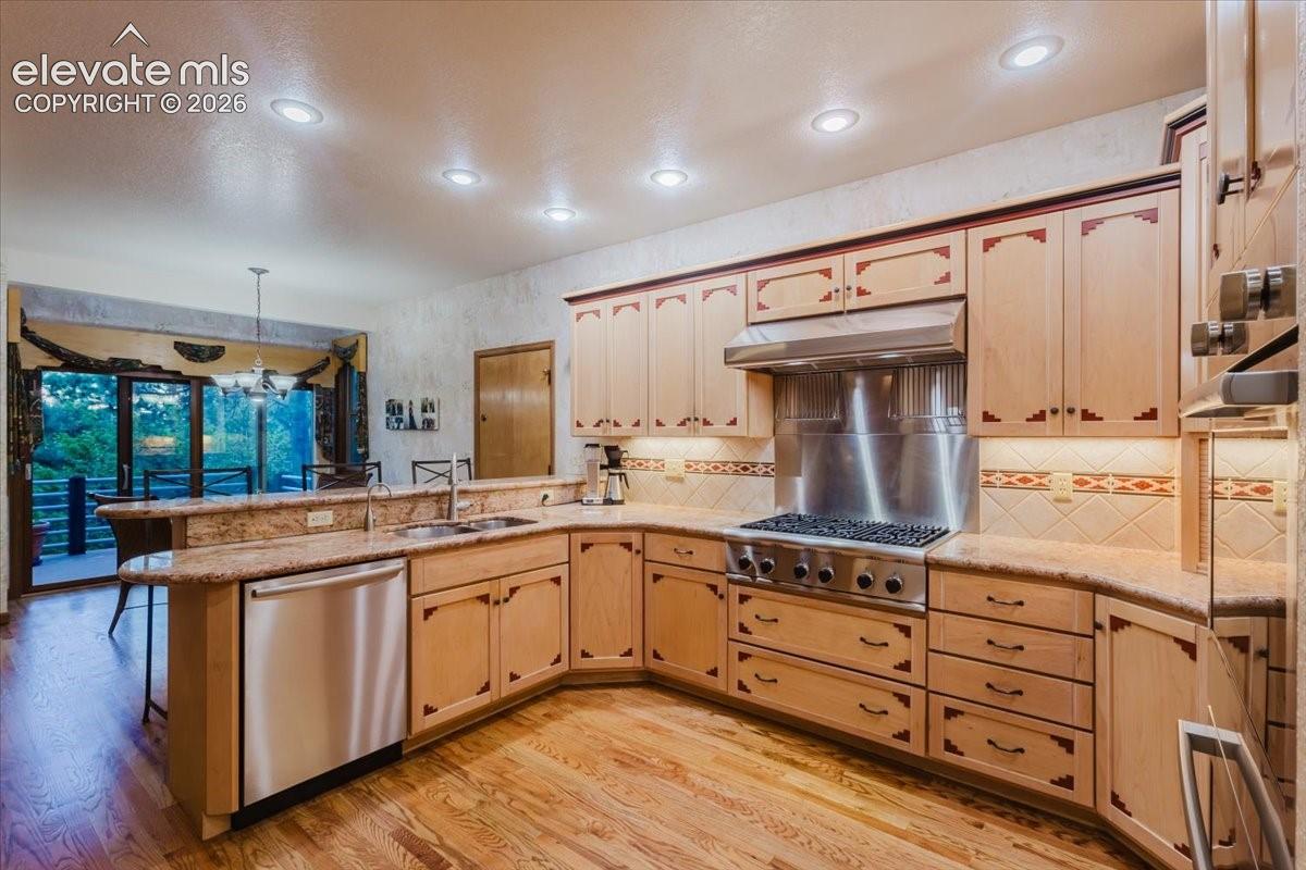U-shaped kitchen featuring light wood cabinetry with decorative inlays, granite countertops, and stainless steel appliances