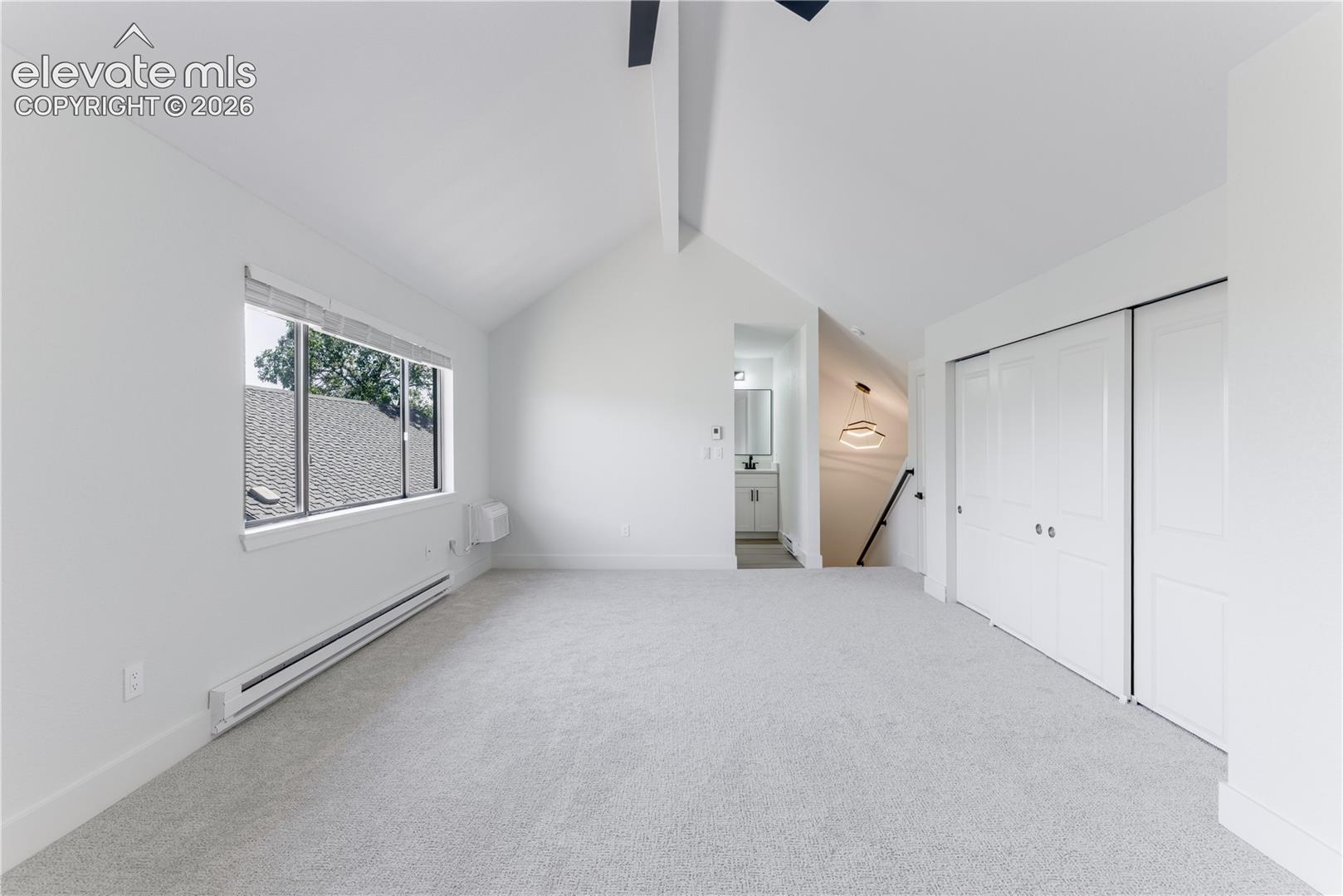 Vaulted ceiling featuring a central exposed beam, neutral wall-to-wall carpeting, and double-door closet storage