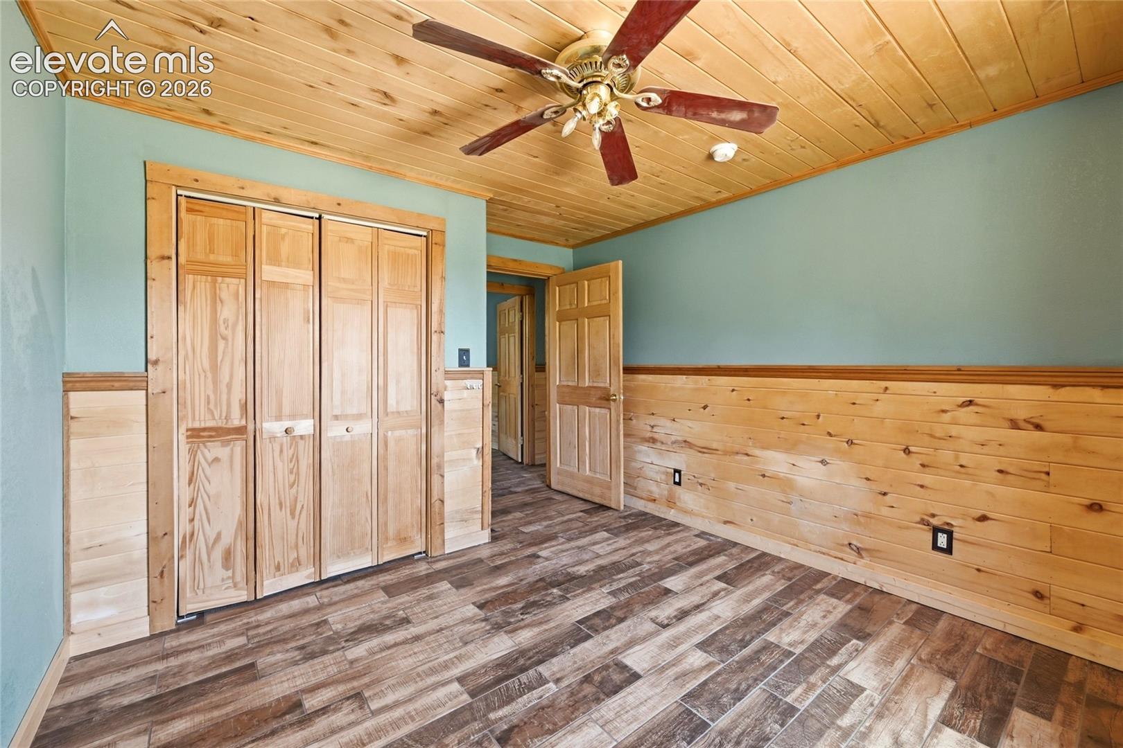 Wood-finish flooring, wood plank ceiling, wood wainscoting, wood bi-fold closet doors, and a ceiling fan