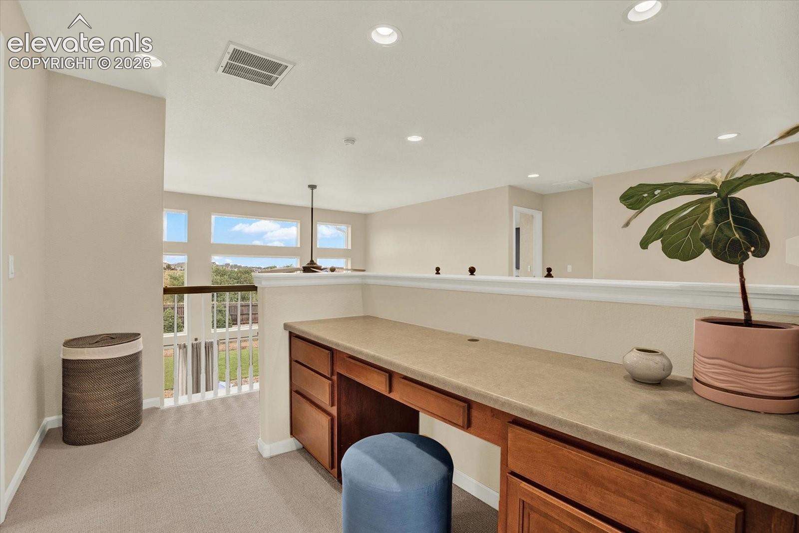 Built-in wooden desk with stone-composite countertop, integrated cabinetry, recessed lighting, carpeted flooring, and multi-pane windows