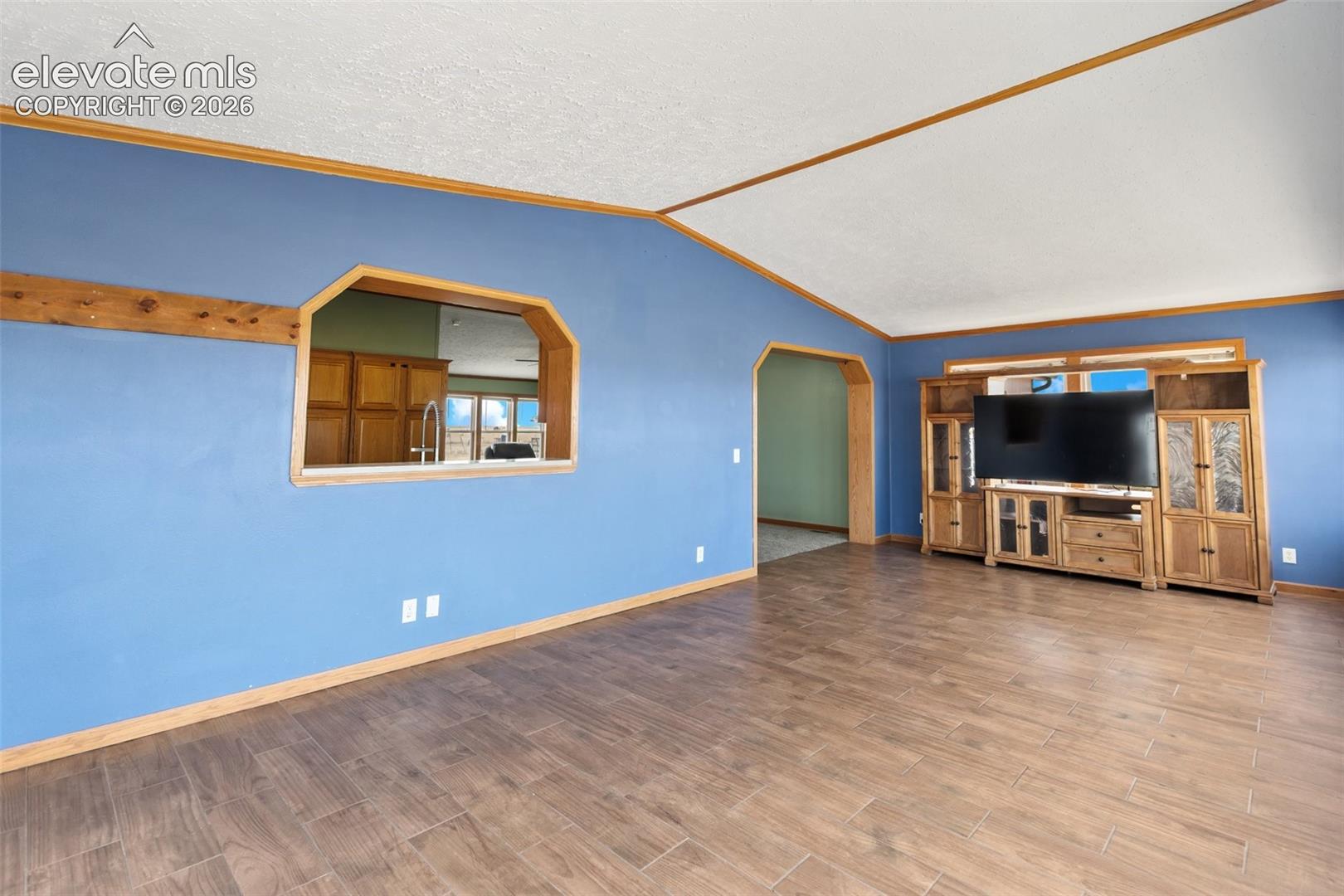 Spacious living area featuring wood-finish flooring, vaulted ceilings, and a pass-through window with wood trim