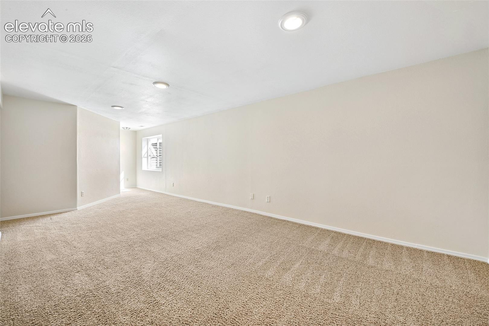 Basement Family Room Neutral-toned walls and plush carpeting, illuminated by recessed ceiling lighting 