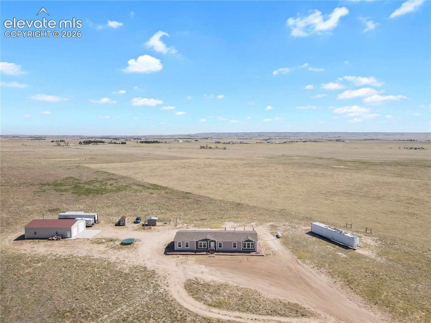 Expansive acreage featuring a single-level residence, a detached multi-car garage with metal roofing, and an elongated storage structure