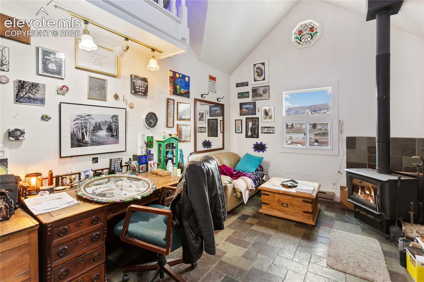 Vaulted ceilings with exposed loft area, stone-tile flooring, wood-burning stove with stone surround, and stained-glass accent window