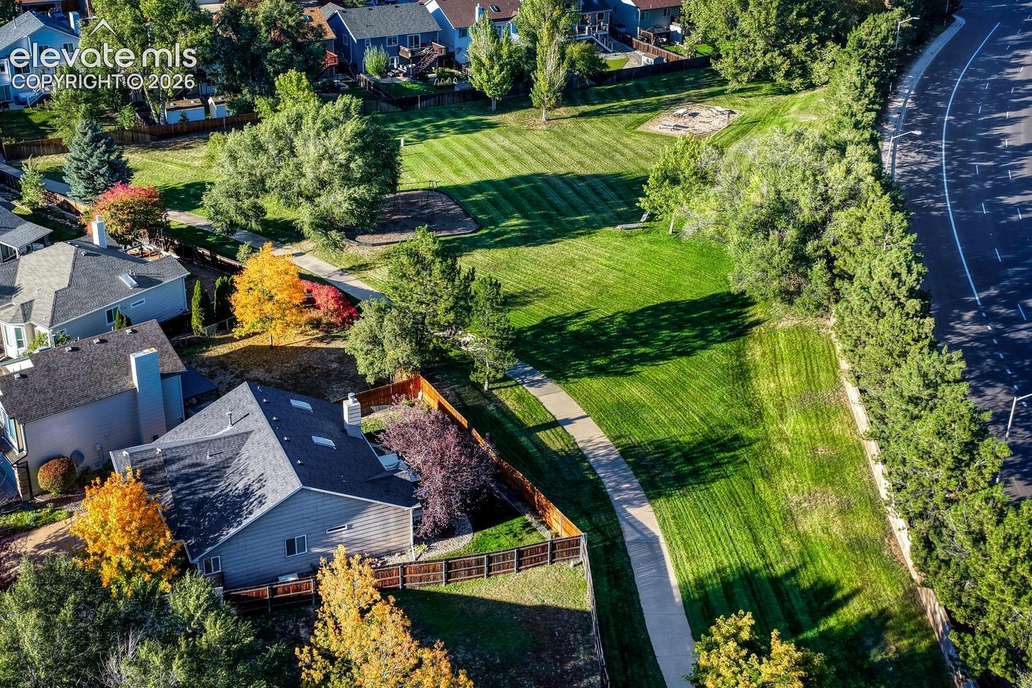 Expansive green space featuring striped lawn, mature trees, and a dedicated play area