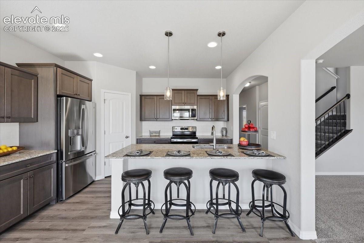 Kitchen featuring dark-toned cabinetry, a stone-surfaced kitchen island with a breakfast bar, recessed lighting, and stainless steel appliances