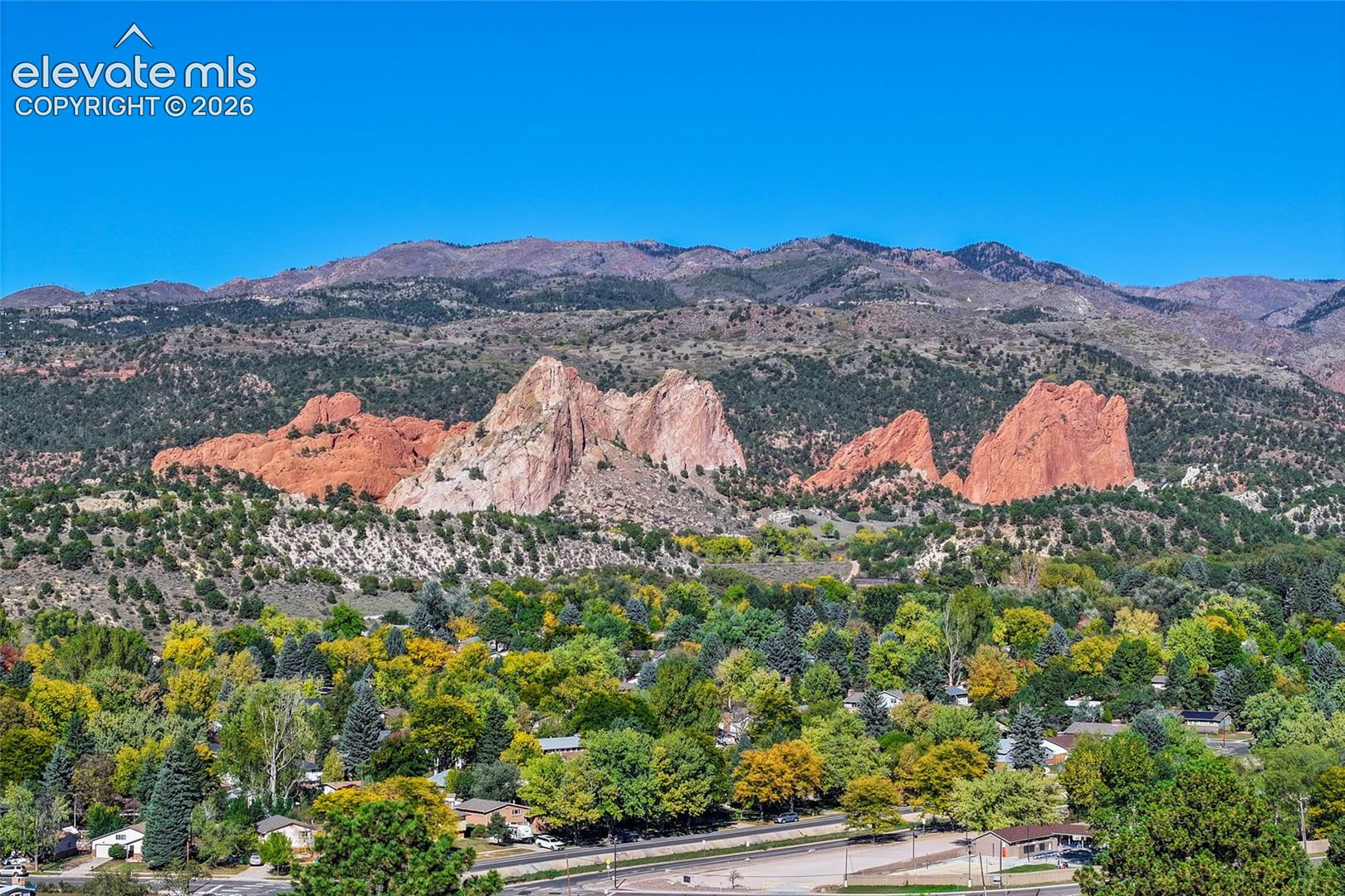 Expansive mountain backdrop featuring prominent red rock formations, rugged peaks, and a densely forested landscape
