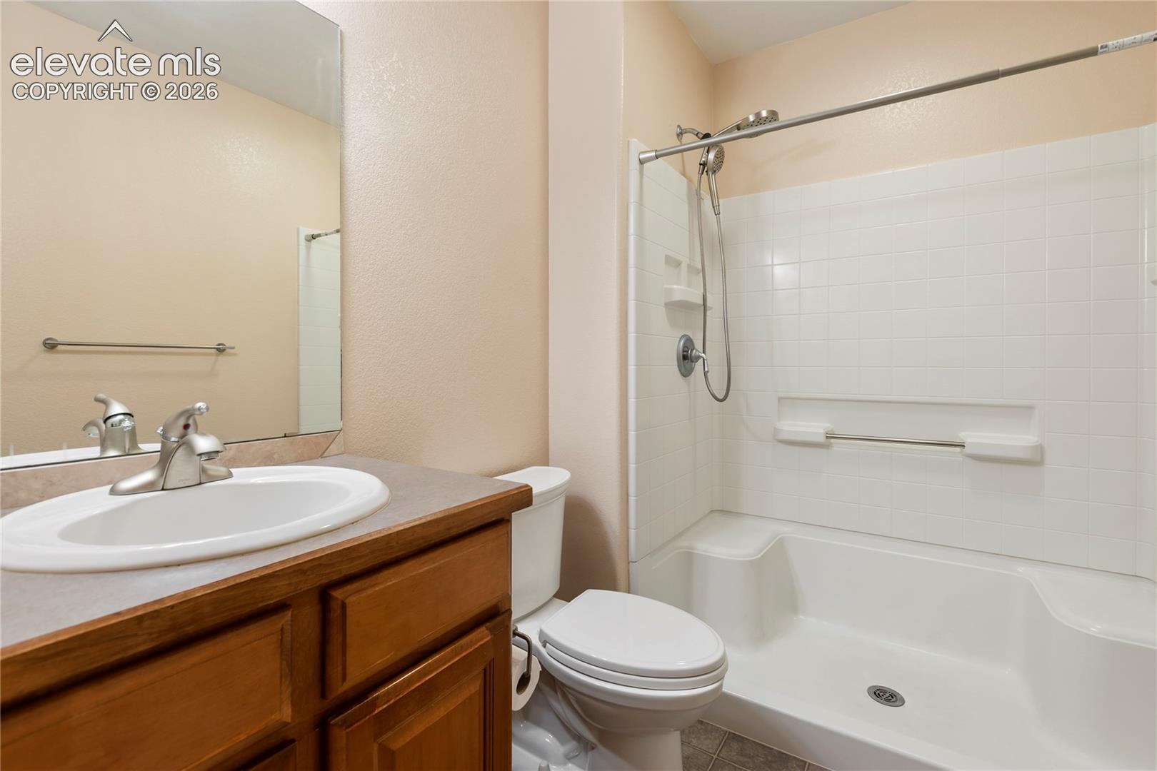 Wood-finish vanity with a drop-in sink, brushed nickel faucet, and a combination shower/tub with white tile surround