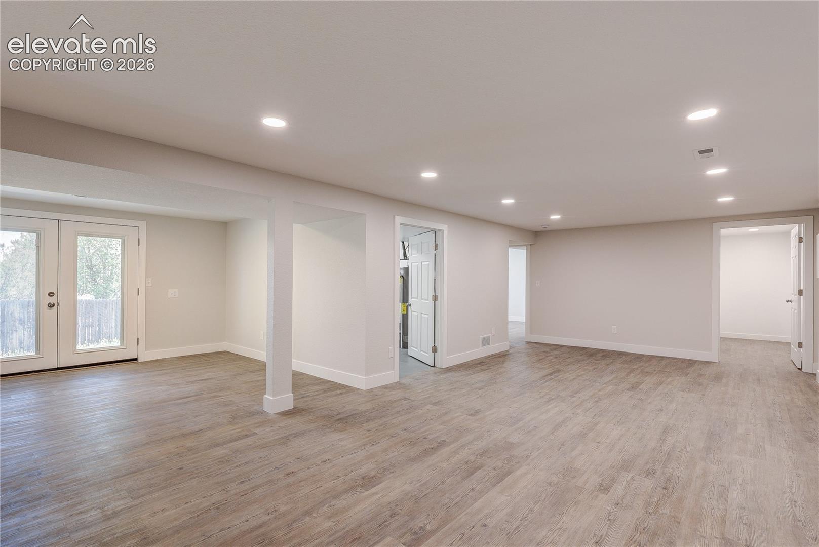 Open-concept interior featuring wood-finish flooring, recessed lighting, and a glass-paneled entry door
