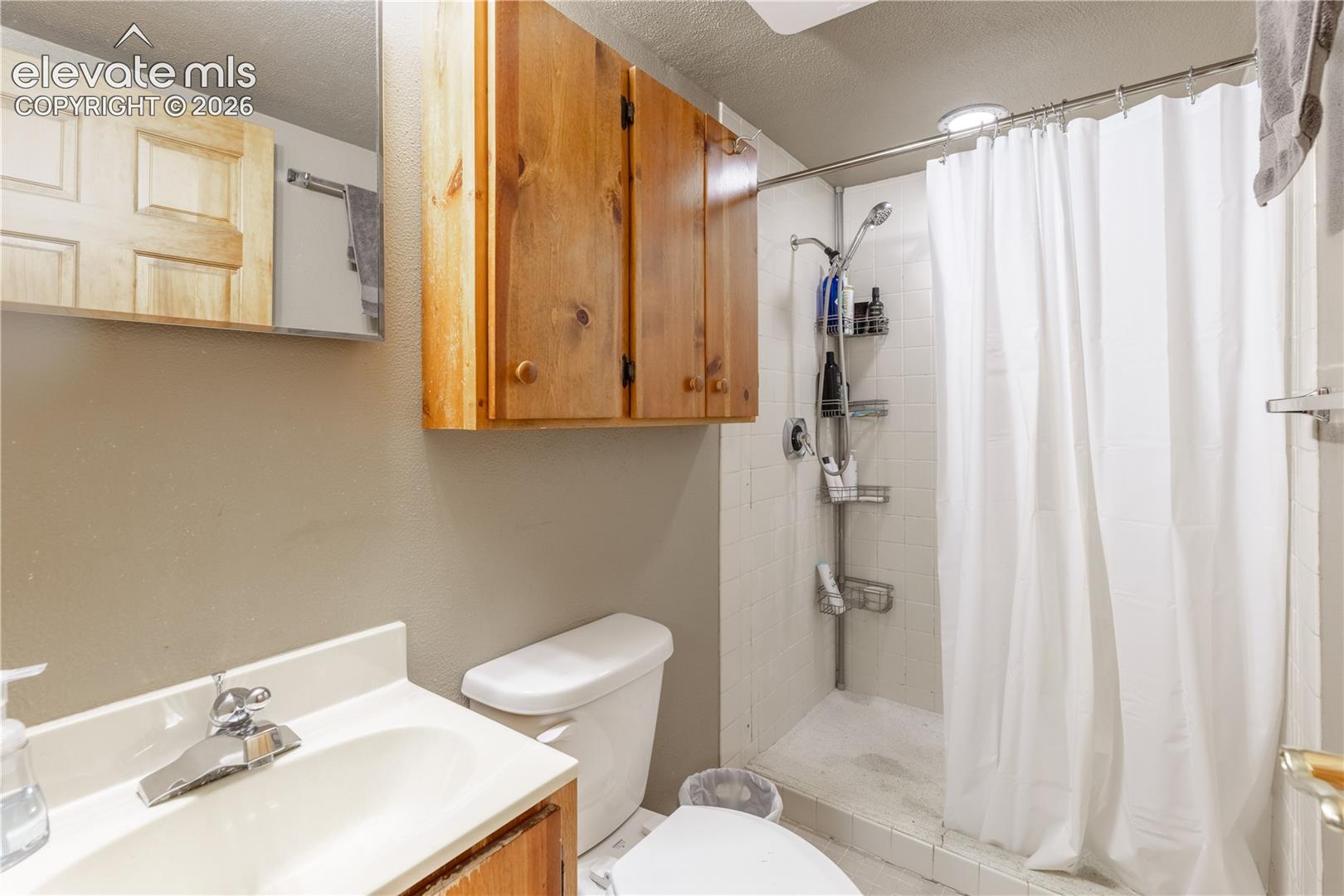 Bathroom featuring wood-finish cabinetry, a white vanity sink, a recessed shower area with tiled surround, and a wall-mounted medicine cabinet