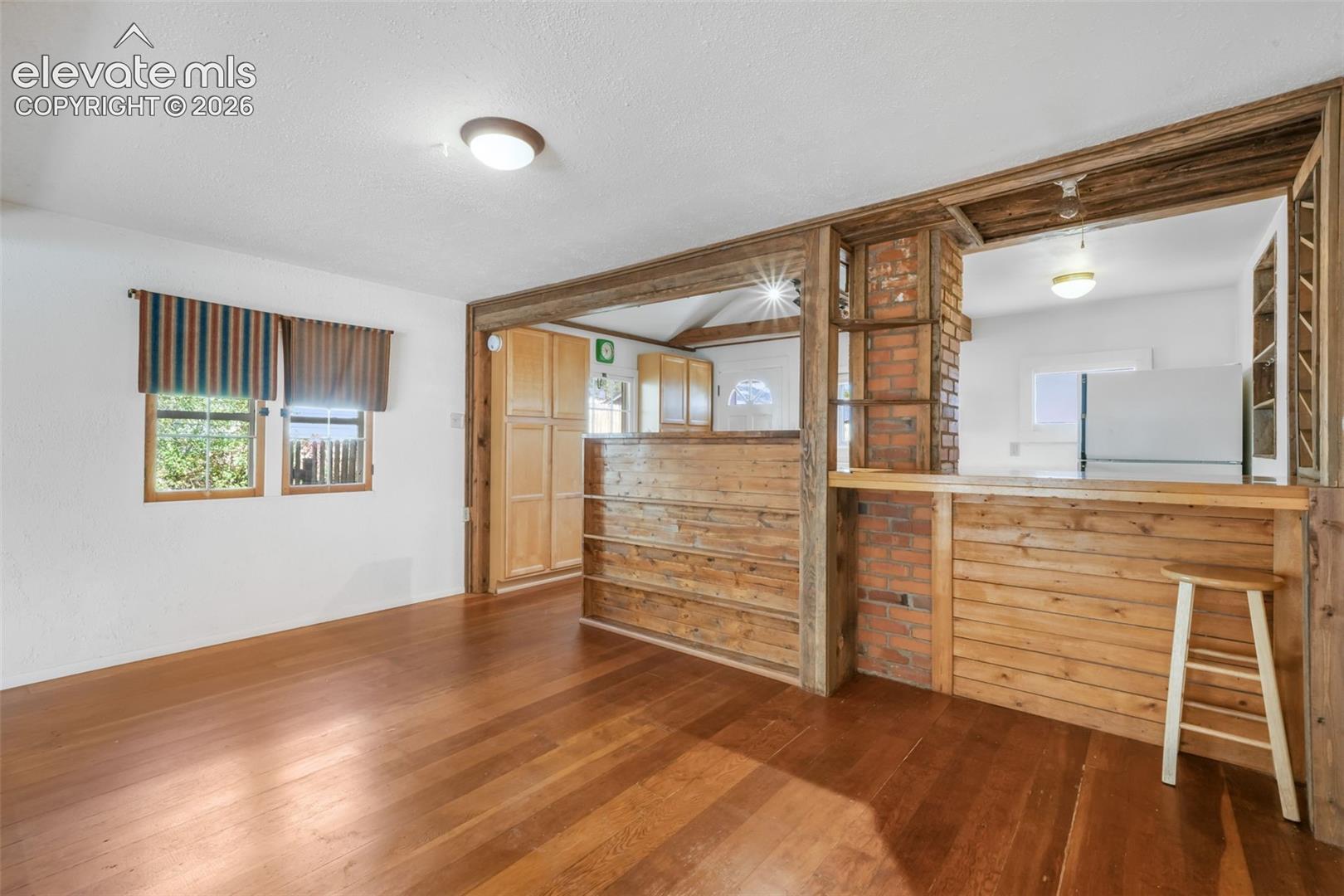 Wood-finish flooring, white walls, and a wood-paneled pass-through with a brick accent