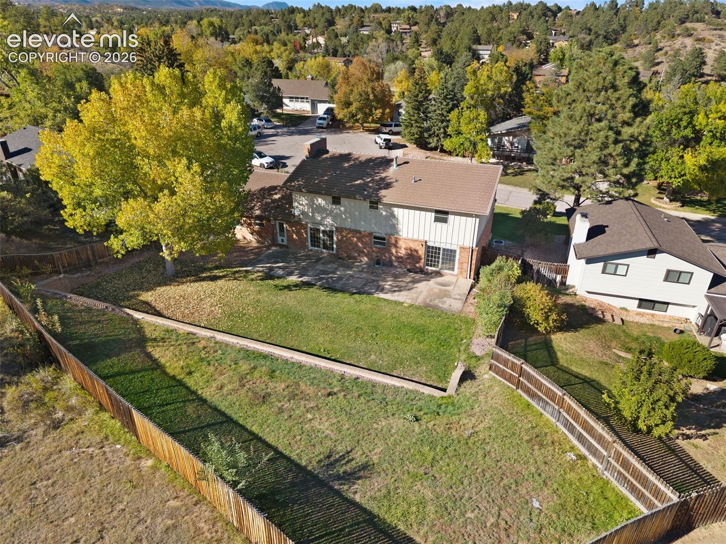 Exterior rear elevation featuring a multi-level lot with a stone retaining wall, paved patio, and fenced perimeter