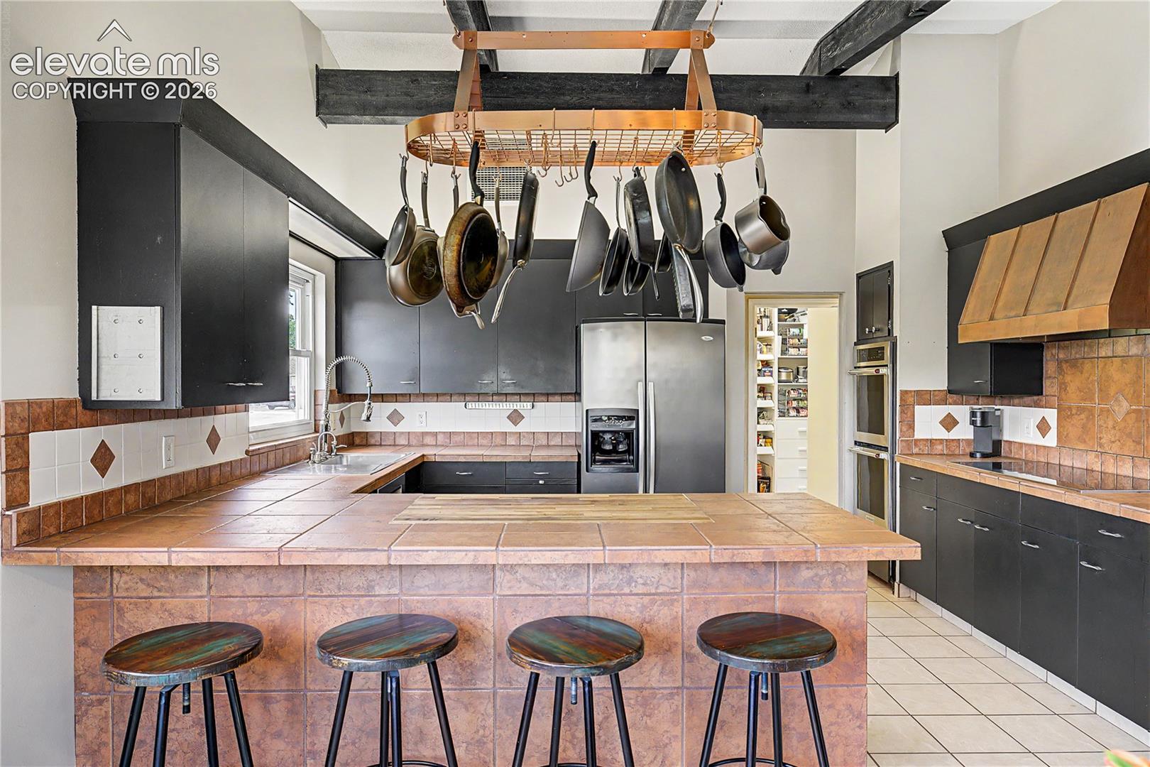 The kitchen's timber-beamed ceiling and hanging pot rack add warmth and character, signaling a space designed for real cooking and gathering.
