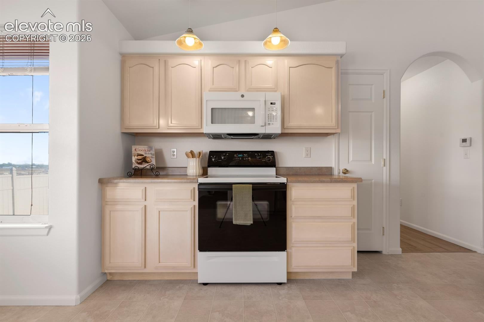 Kitchen featuring light-toned cabinetry, solid-surface countertops, built-in microwave, range, and pendant lighting