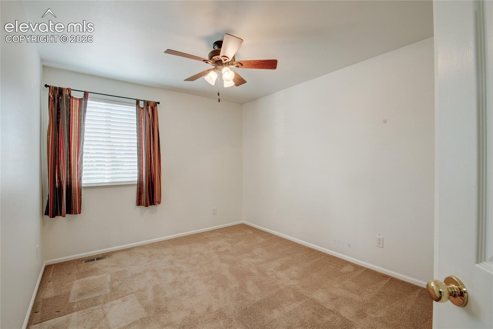 Neutral-toned room with a ceiling fan light fixture, beige wall-to-wall carpeting, and a window featuring horizontal blinds