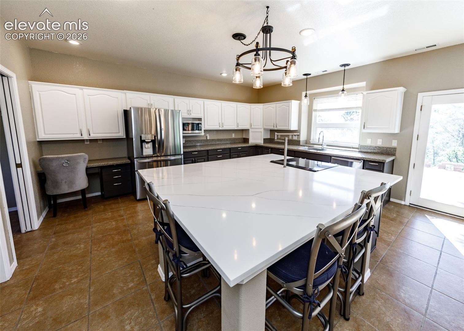 Oversized kitchen island with quartz countertops, custom two-tone cabinetry, stainless steel appliances, tile flooring, and decorative metal chandelier