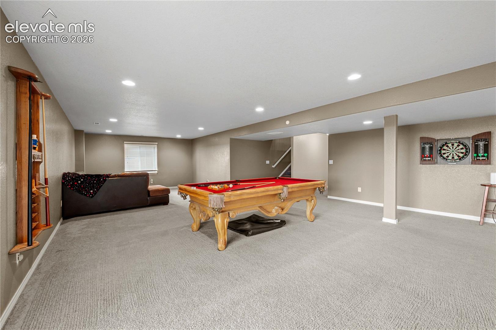 Spacious entertainment area featuring recessed lighting, light-colored carpeting, and a built-in wooden cue rack
