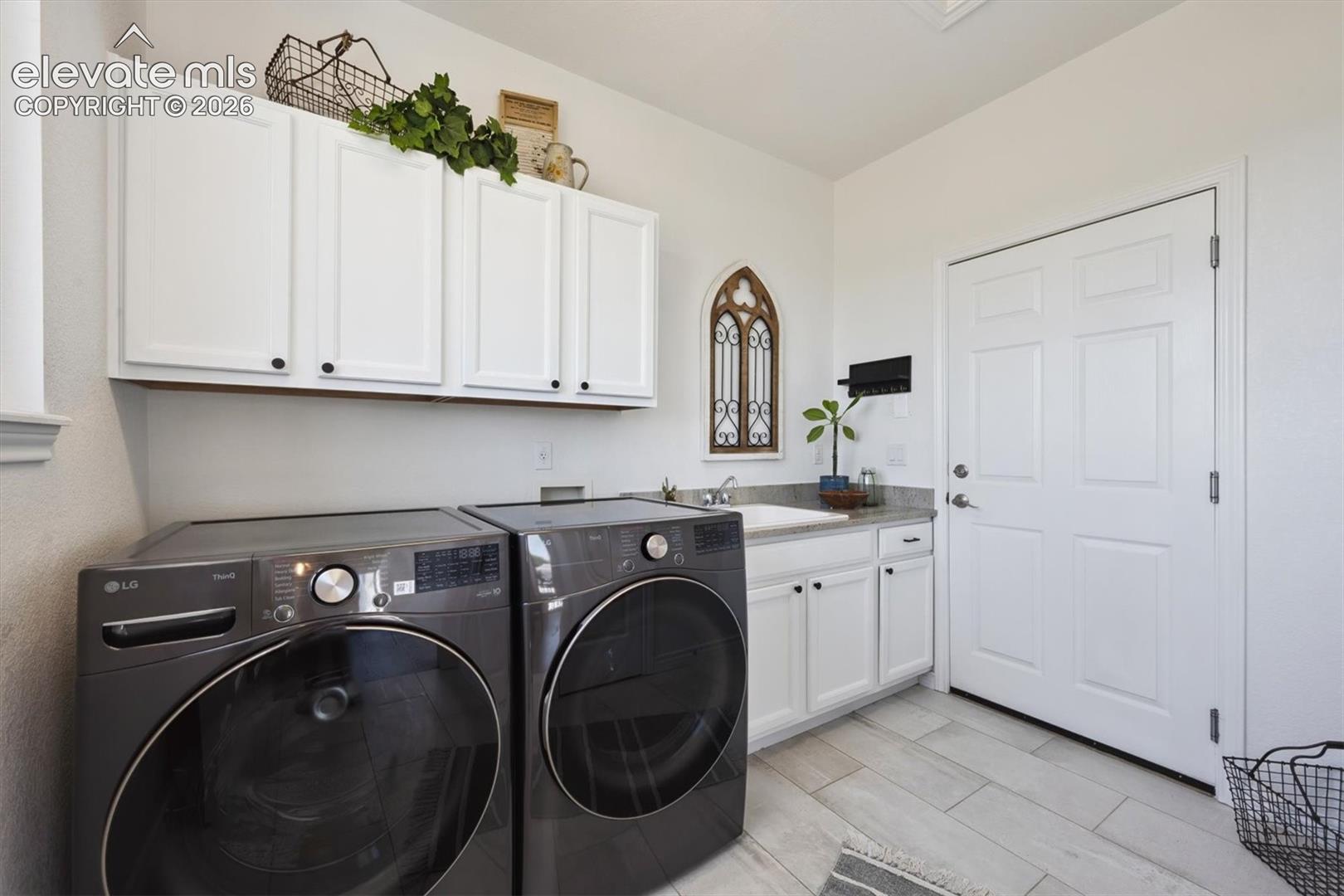 Functional laundry space featuring light-toned flooring, white cabinetry, a built-in sink, and a contrasting countertop