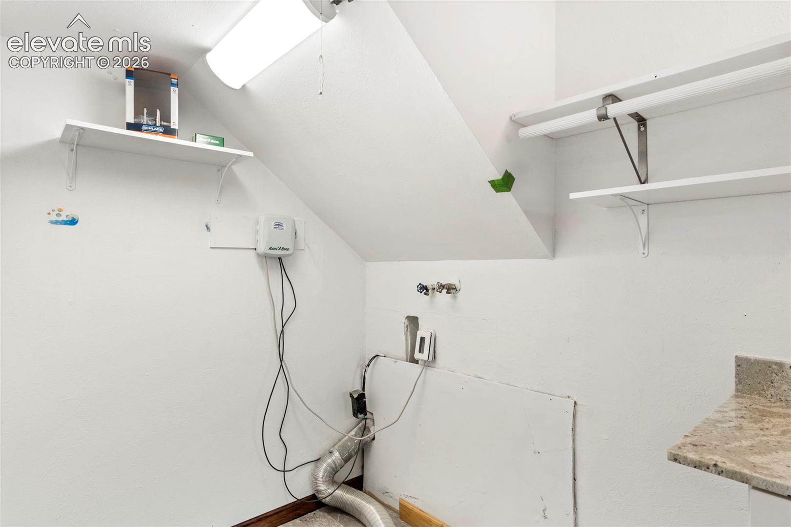 Utility area featuring multiple storage shelves, a ceiling-mounted fluorescent light fixture, and a stone-finish countertop