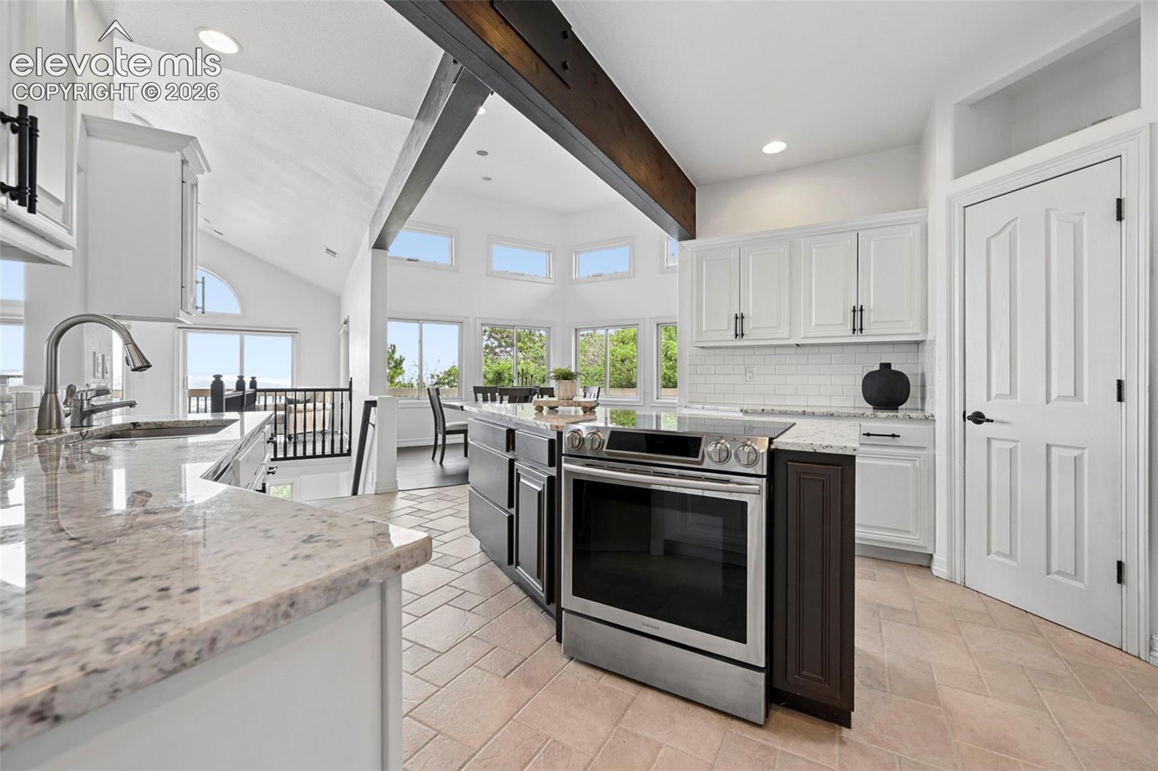 Kitchen featuring a stainless steel range, white shaker-style cabinetry, light-toned stone countertops, and a subway tile backsplash