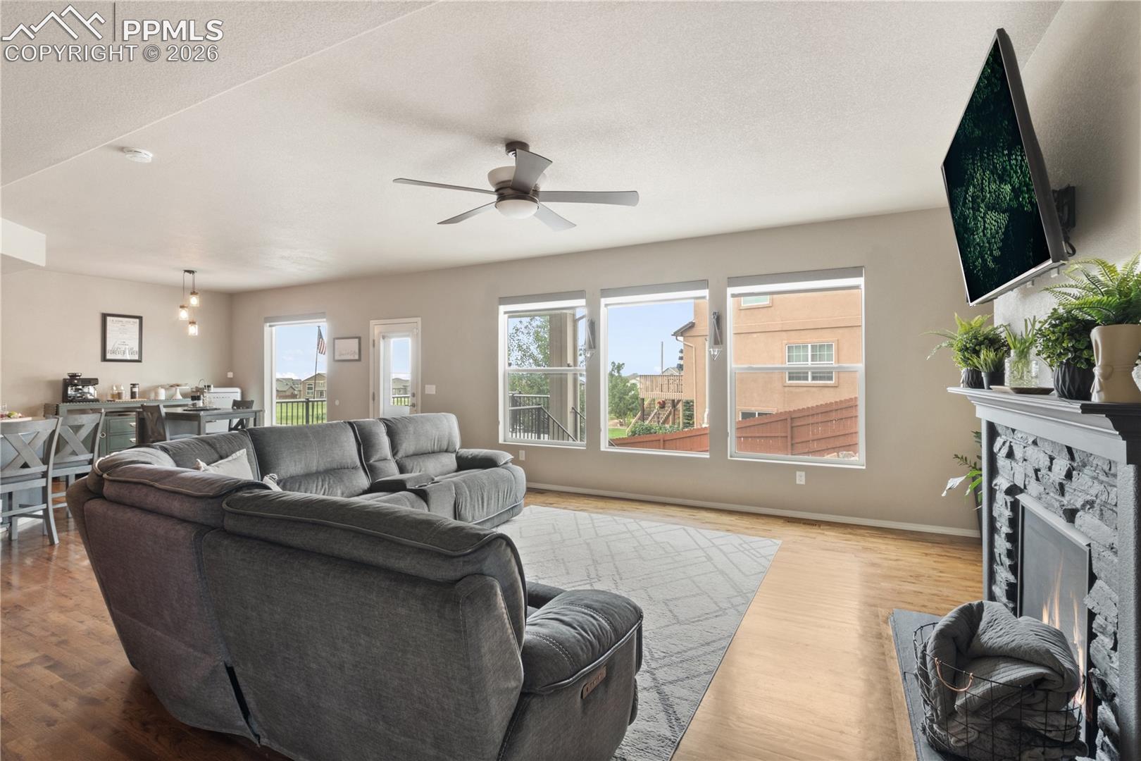 Living room with wood finished floors, a stone fireplace, ceiling fan, and a textured ceiling