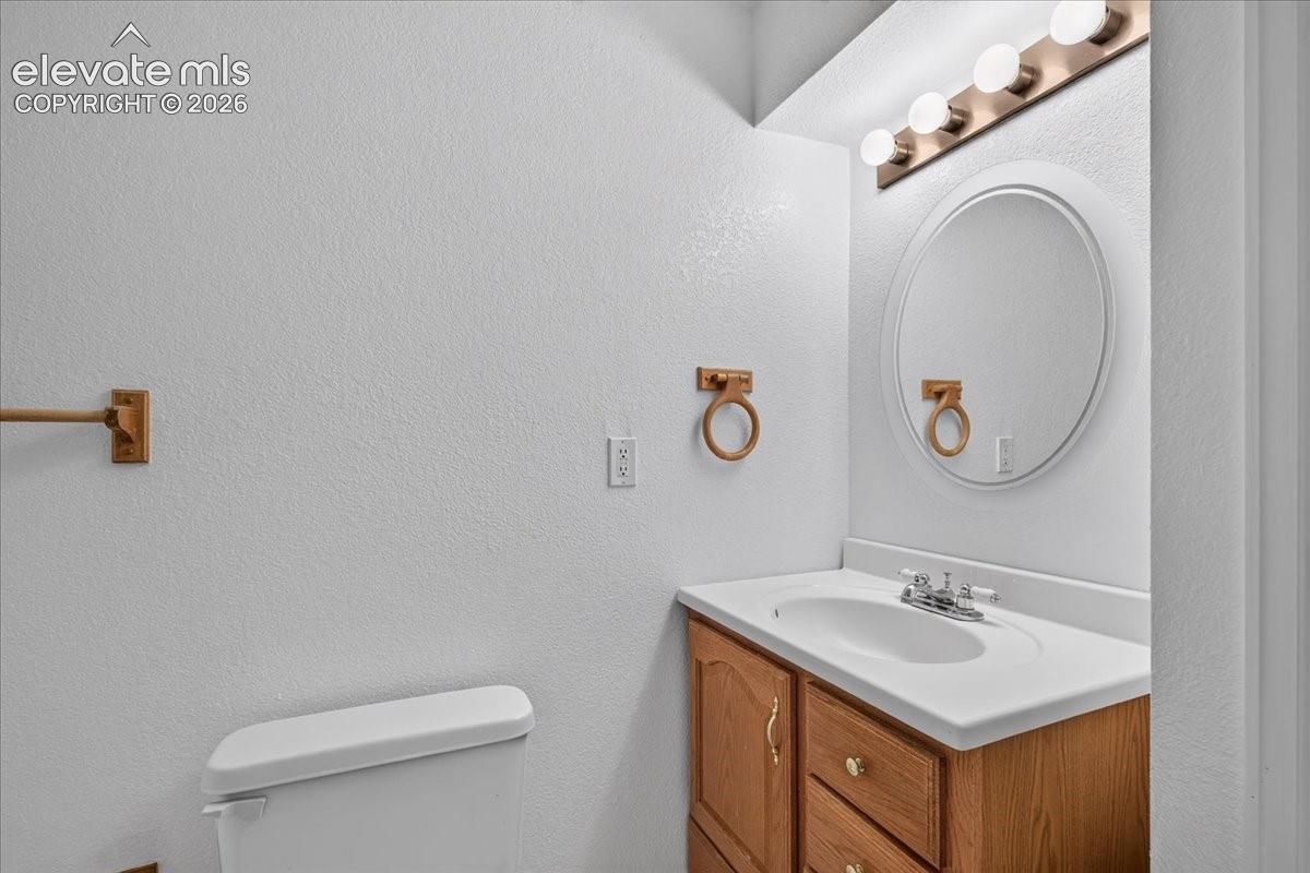 Vanity featuring a light wood cabinet, integrated molded sink, circular mirror, and multi-bulb vanity light fixture