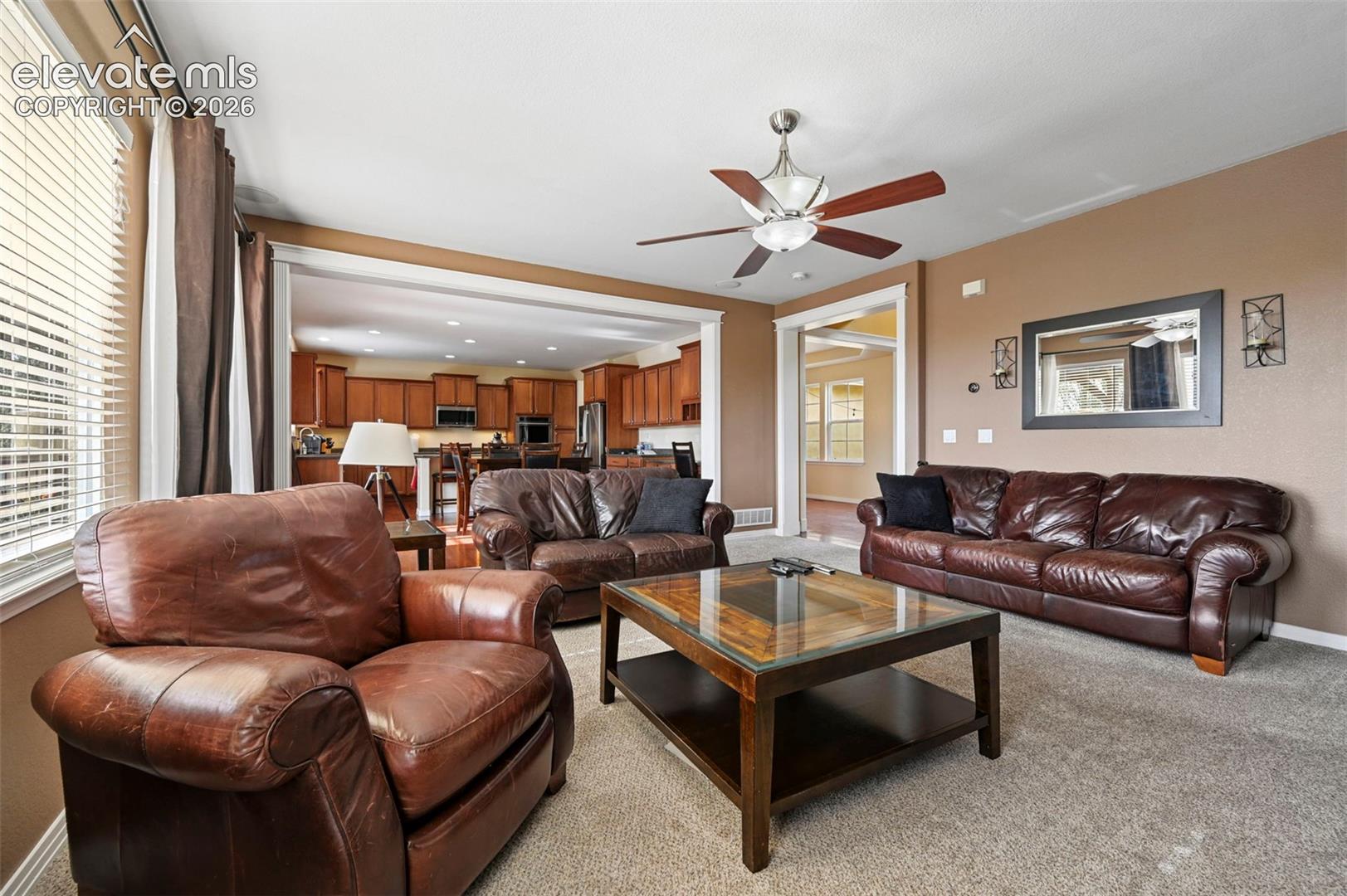 Living area with neutral carpeting, an overhead ceiling fan, and a wide cased opening to an additional room