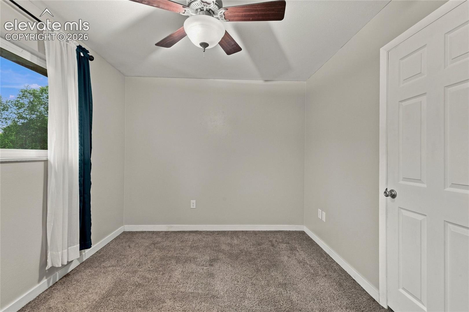 Spacious primary bedroom featuring walk-in closet, carpet flooring, a ceiling fan with integrated lighting, and large windows with dual-layer window treatments