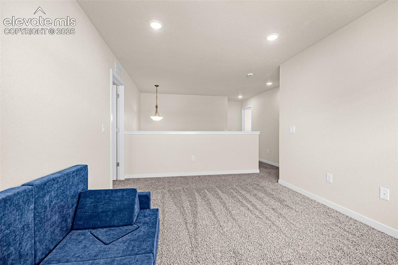Recessed ceiling lighting illuminates a spacious room featuring neutral-toned textured walls and plush carpet flooring
