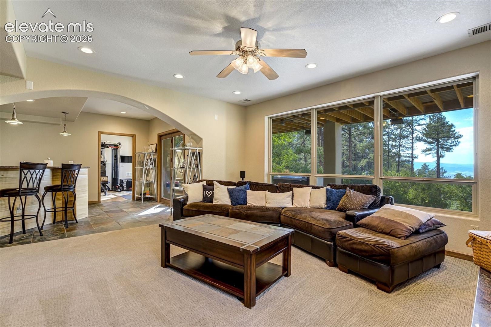 Recessed lighting throughout, arched doorway, built-in bar with pendant lights, large windows, and a ceiling fan
