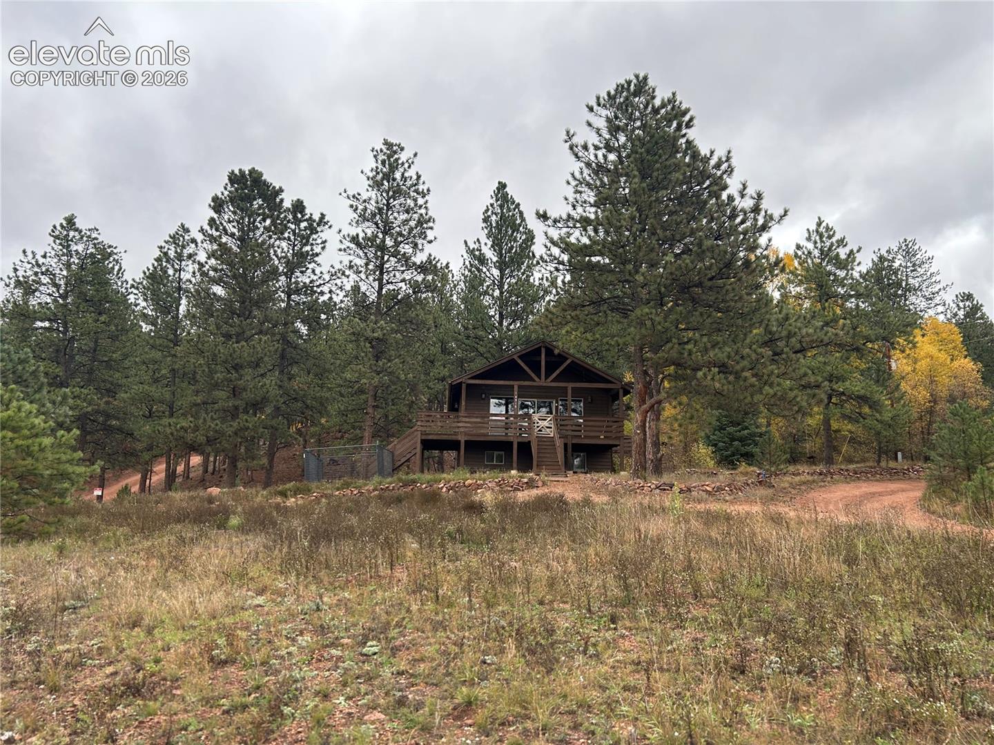Wood-sided home exterior featuring a multi-level wooden deck, stone foundation, and mature evergreen trees on a natural landscape