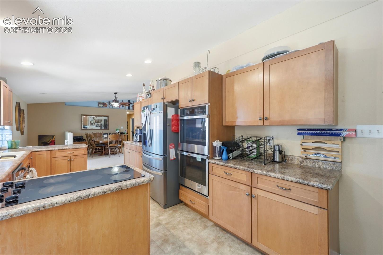 Kitchen featuring light wood cabinetry, stone-look countertops, stainless steel appliances, and a built-in double oven