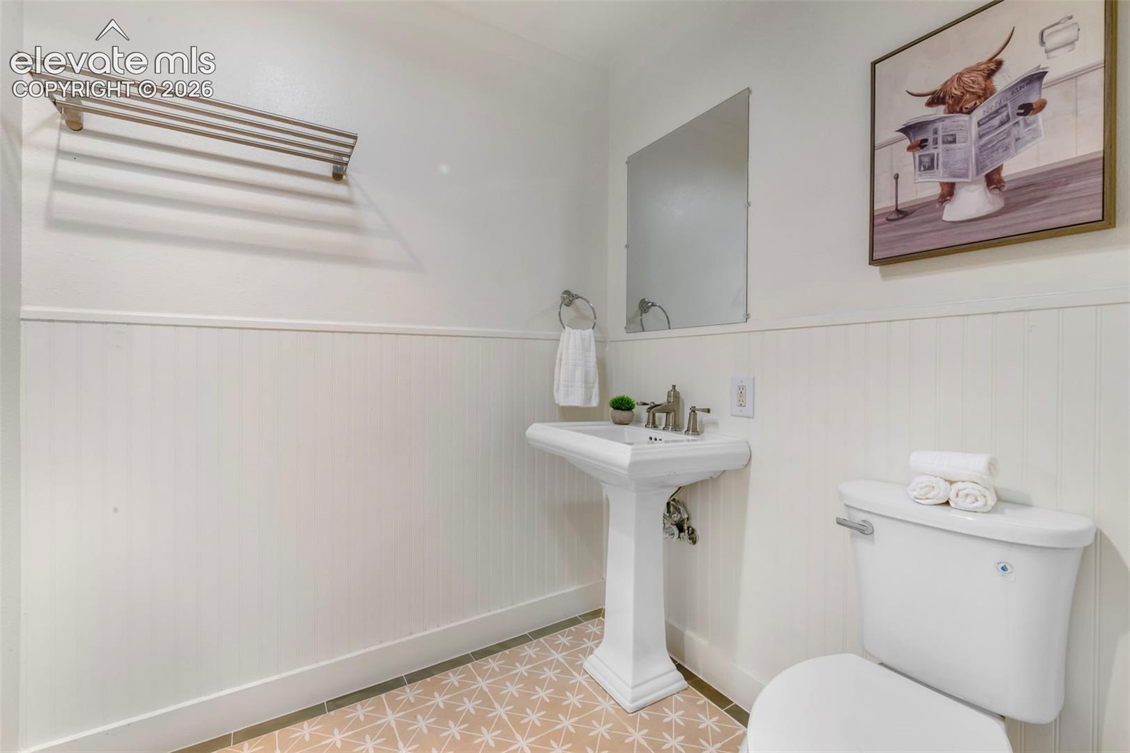 Pedestal sink with a polished metal faucet, wall-mounted towel rack, beadboard wainscoting, and patterned tile flooring