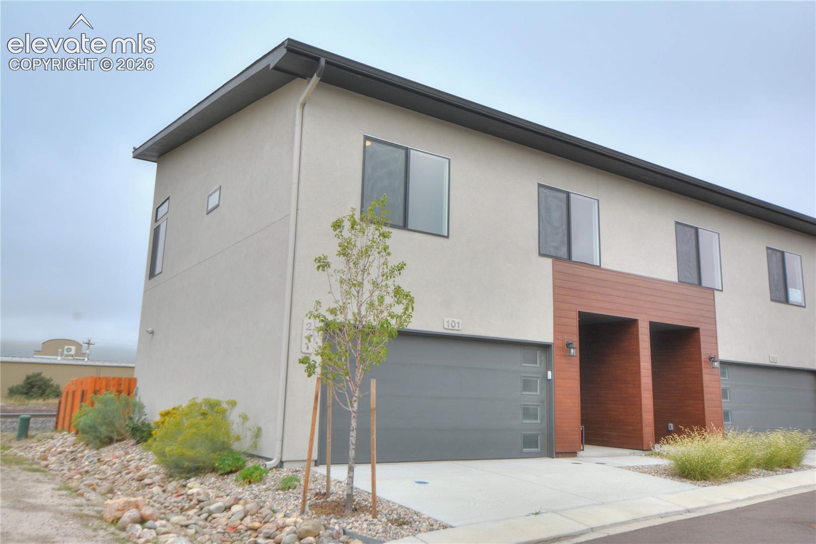 Modern stucco exterior with flat roofline, integrated garage, wood-finish facade elements, and contemporary windows