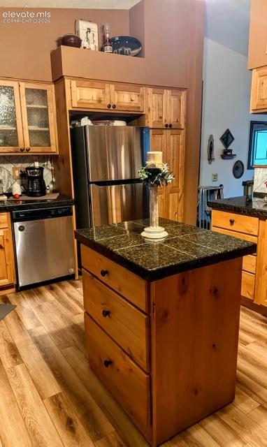 Kitchen featuring a central island with a tiled countertop, stainless steel appliances, wood-finish cabinetry, and wood-look flooring