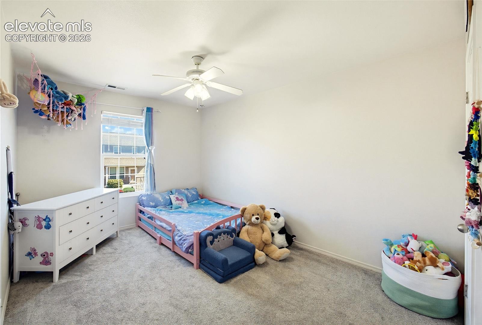 Bright secondary bedroom featuring carpeted flooring, a ceiling fan with integrated lighting, and large window with natural light