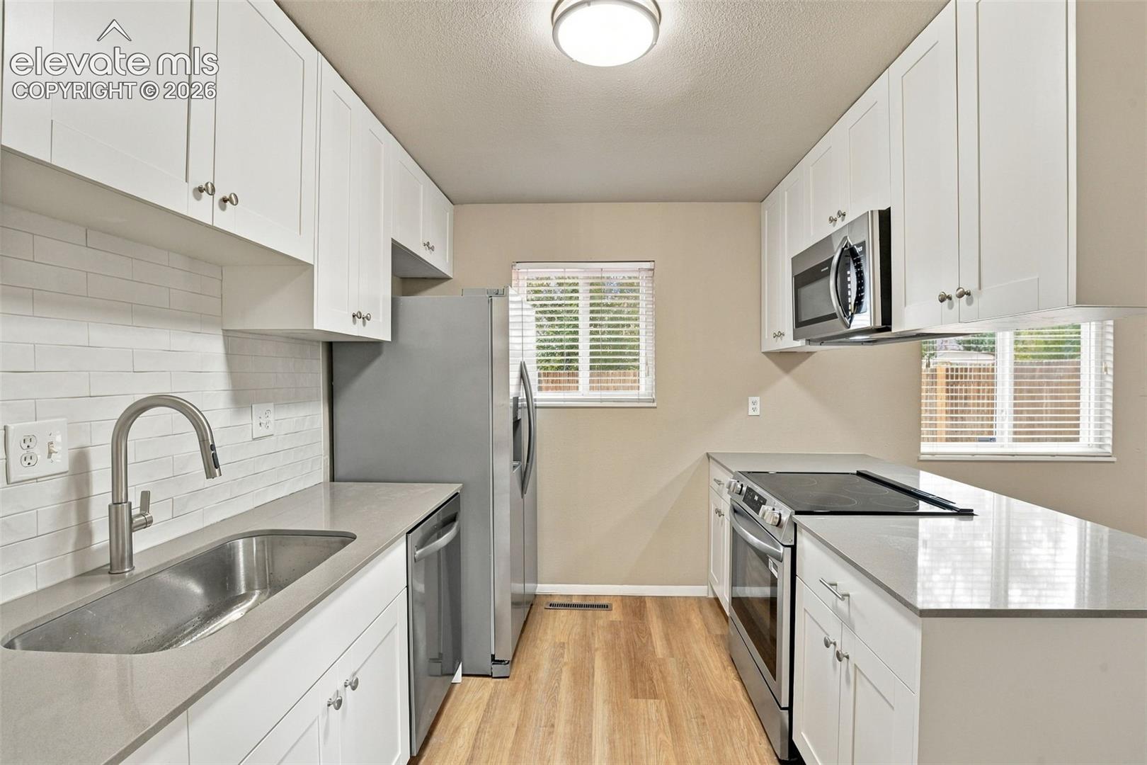 Kitchen featuring white cabinetry, solid-surface countertops, horizontal tile backsplash, stainless steel appliances, and wood-finish flooring