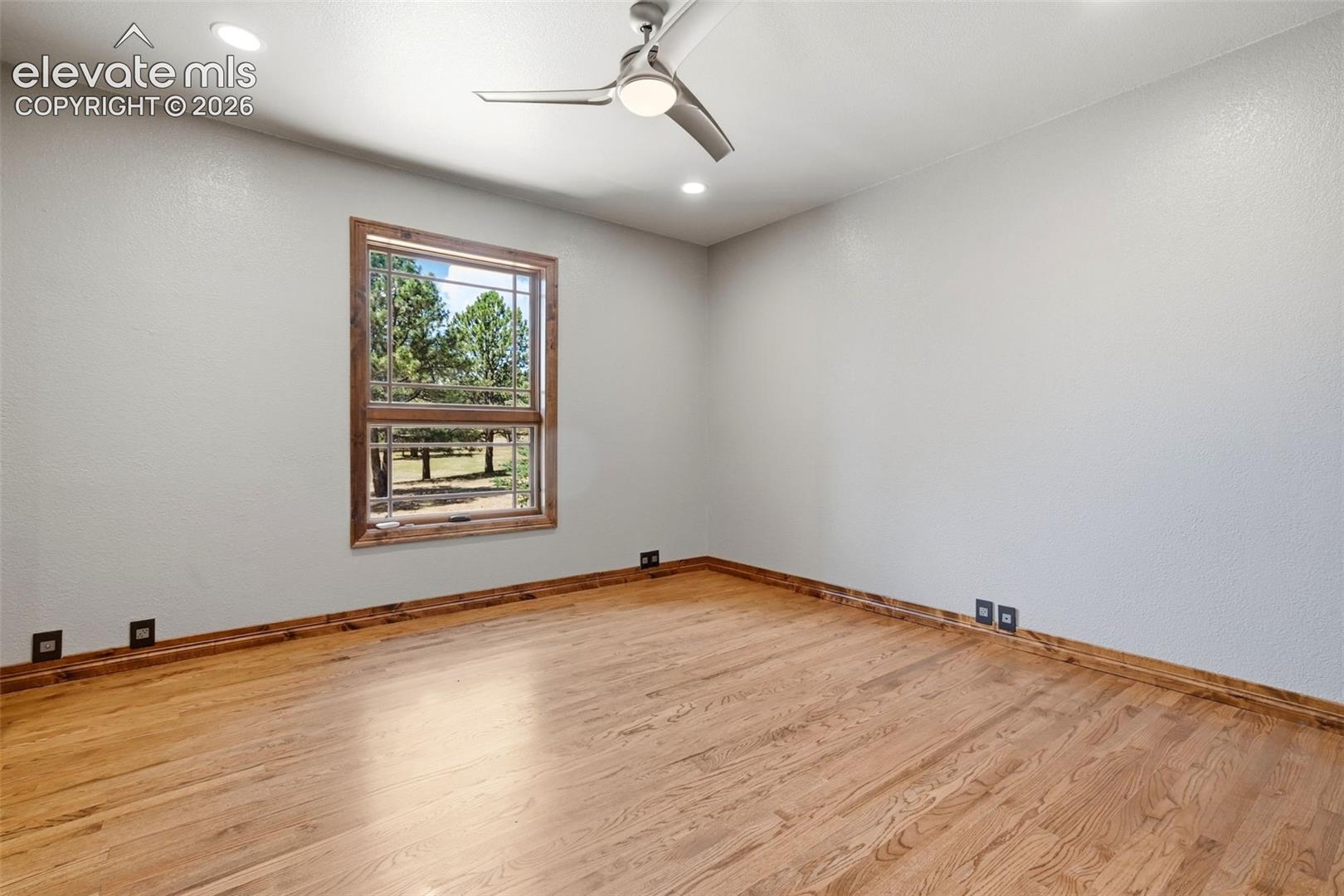 Room featuring warm wood-finish flooring, a large window with natural wood trim, recessed lighting, and a ceiling fan with integrated illumination