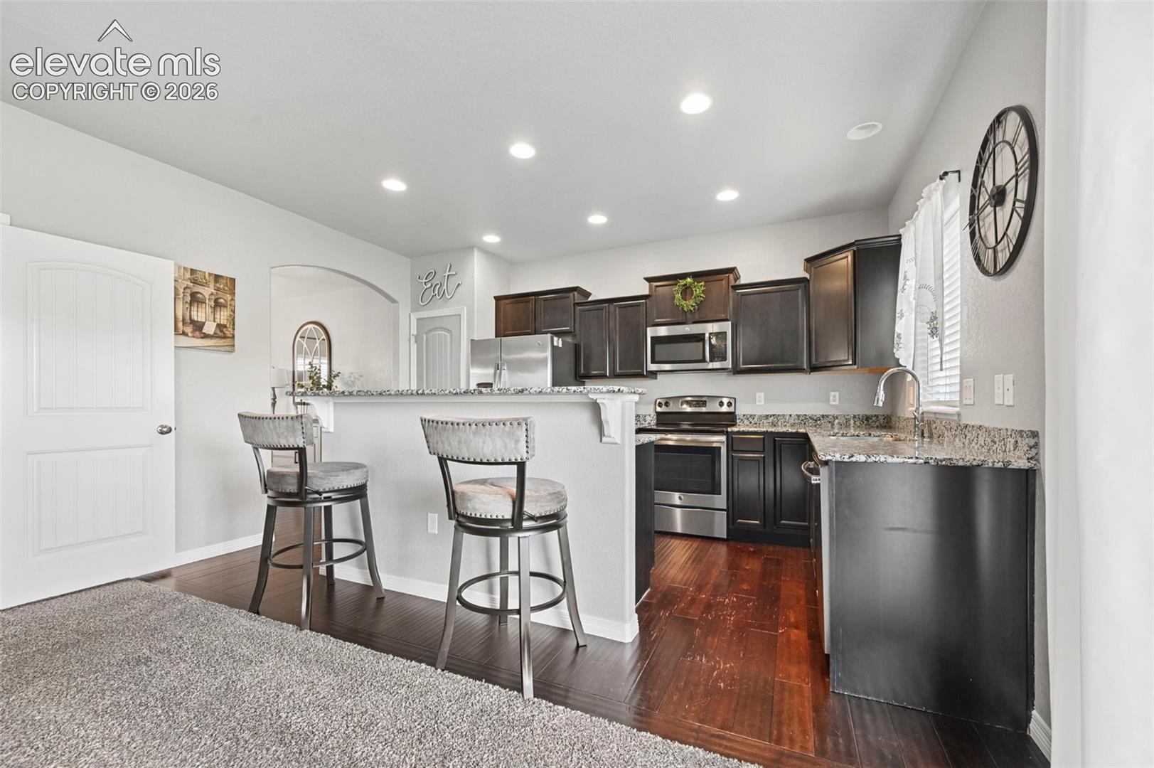Kitchen featuring dark wood-finish cabinetry, stainless steel appliances, speckled countertops, and recessed lighting