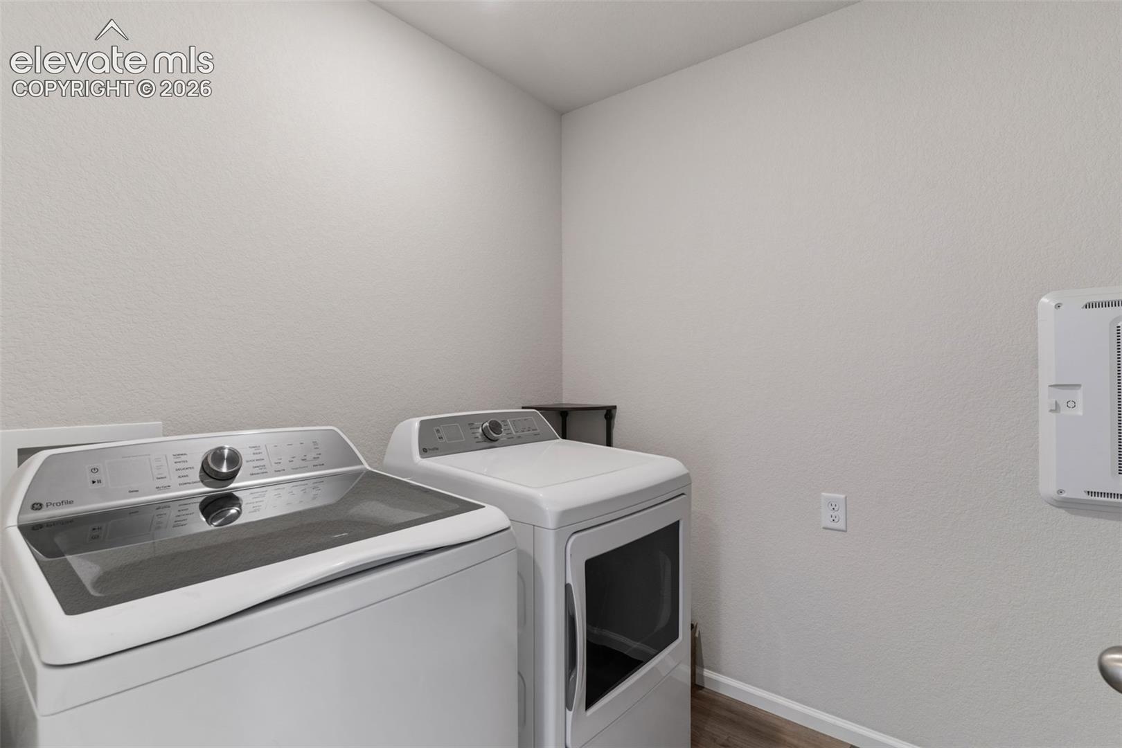 Dedicated laundry area featuring light-toned walls, wood-finish flooring, and a white washer and dryer set