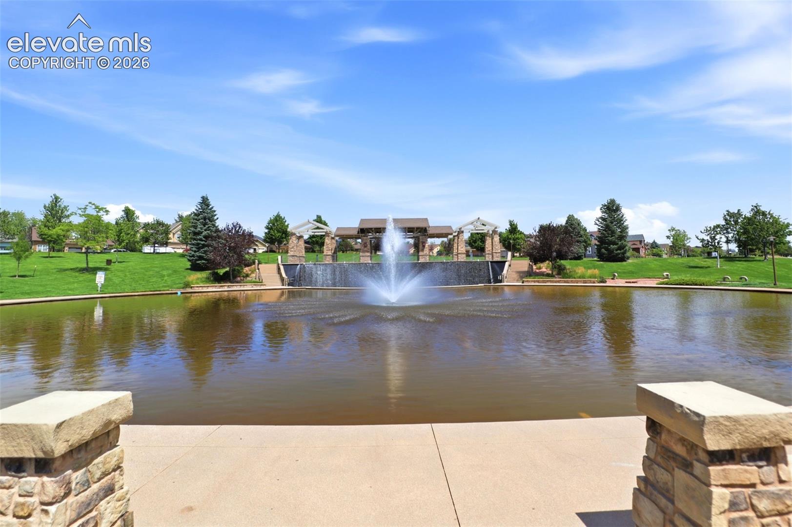 Community pond with a central fountain feature, expansive green spaces, and stone-clad architectural elements