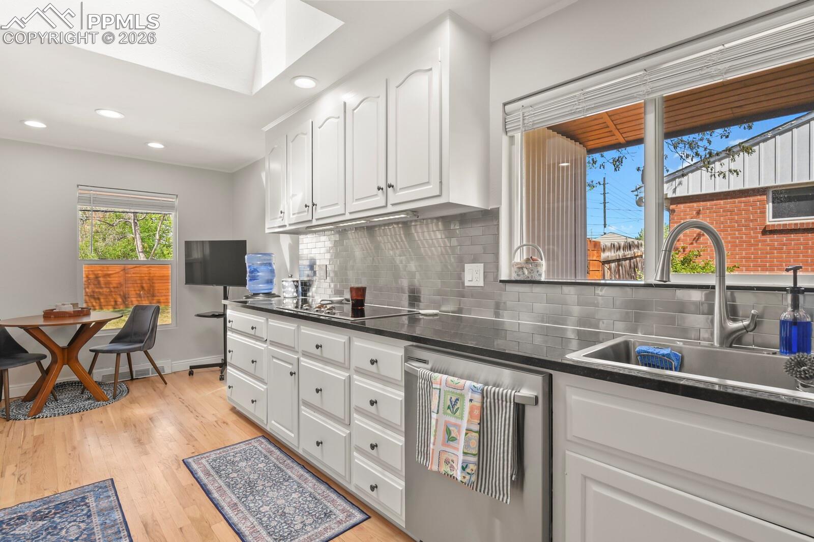Kitchen featuring white cabinetry, hardwood floors, stainless subway tile backsplash and a breakfast nook.