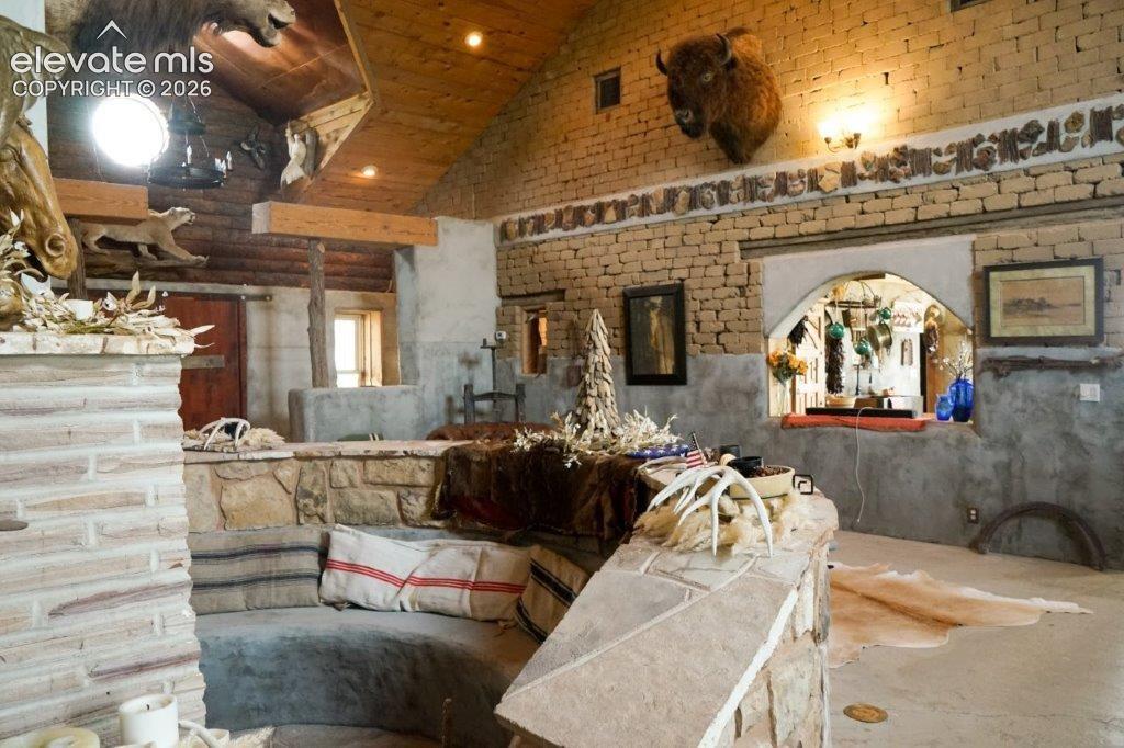Living Room/Great Room with architectural interior featuring, the sunken stone sitting area, adobe bring walls, a wood-plank vaulted ceiling with recessed lighting and bypass opening to the kitchen