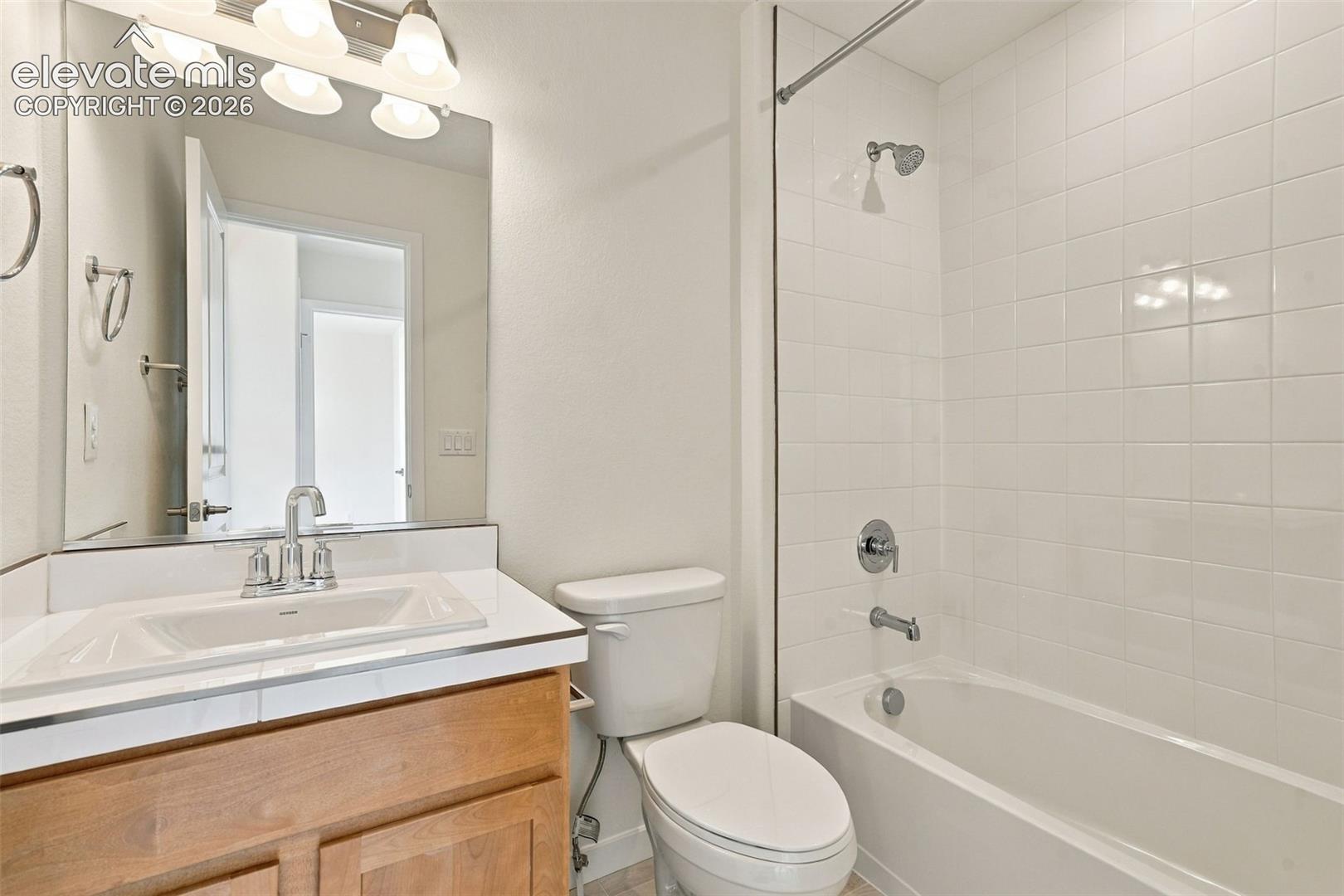 Bathroom featuring a wood-finish vanity with an integrated sink, a large wall-mounted mirror, and a tiled shower/tub combination with a chrome showerhead