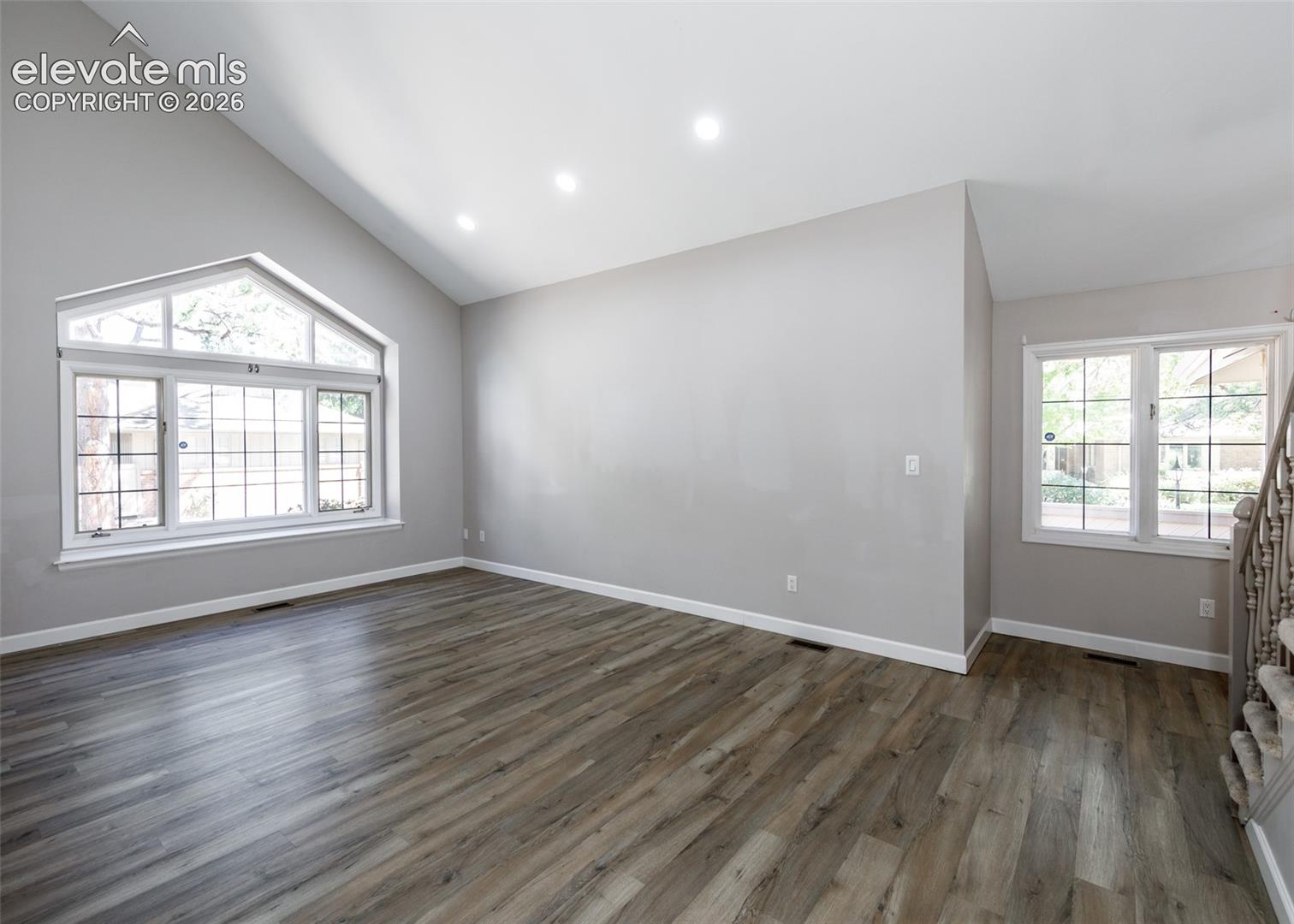 Vaulted ceiling with recessed lighting, wood-finish flooring, and a large arched window