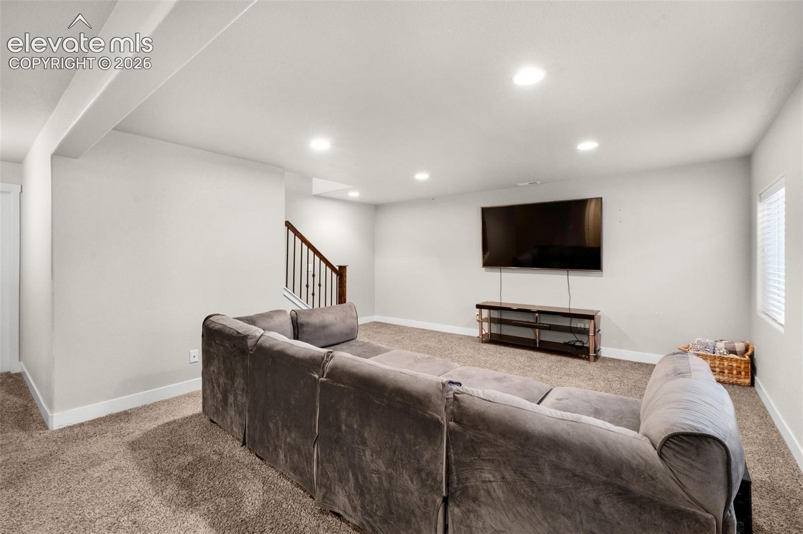 Neutral-toned interior space featuring recessed ceiling lighting, wall-to-wall carpeting, and a staircase with a wooden handrail and balusters
