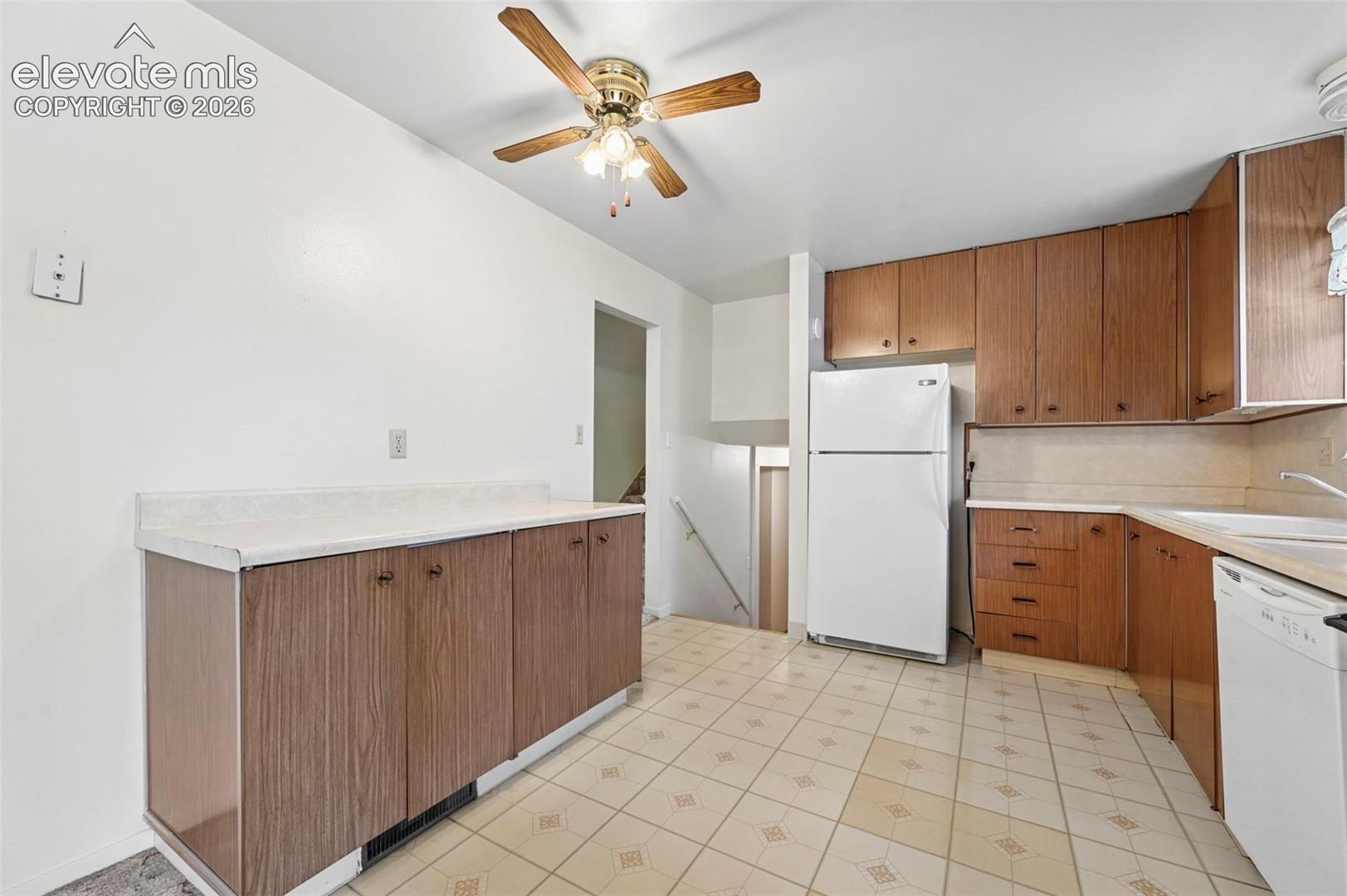 Kitchen featuring wood-finish cabinetry, solid surface countertops, a white refrigerator, a dishwasher, and a ceiling-mounted light fixture with a fan