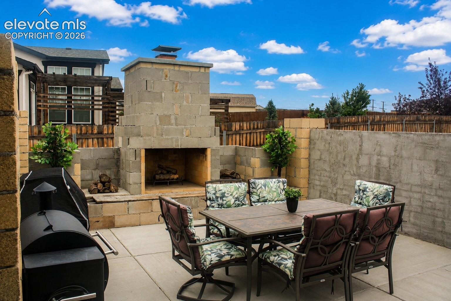 Expansive concrete patio featuring a built-in outdoor fireplace, concrete block construction, and a solid privacy wall