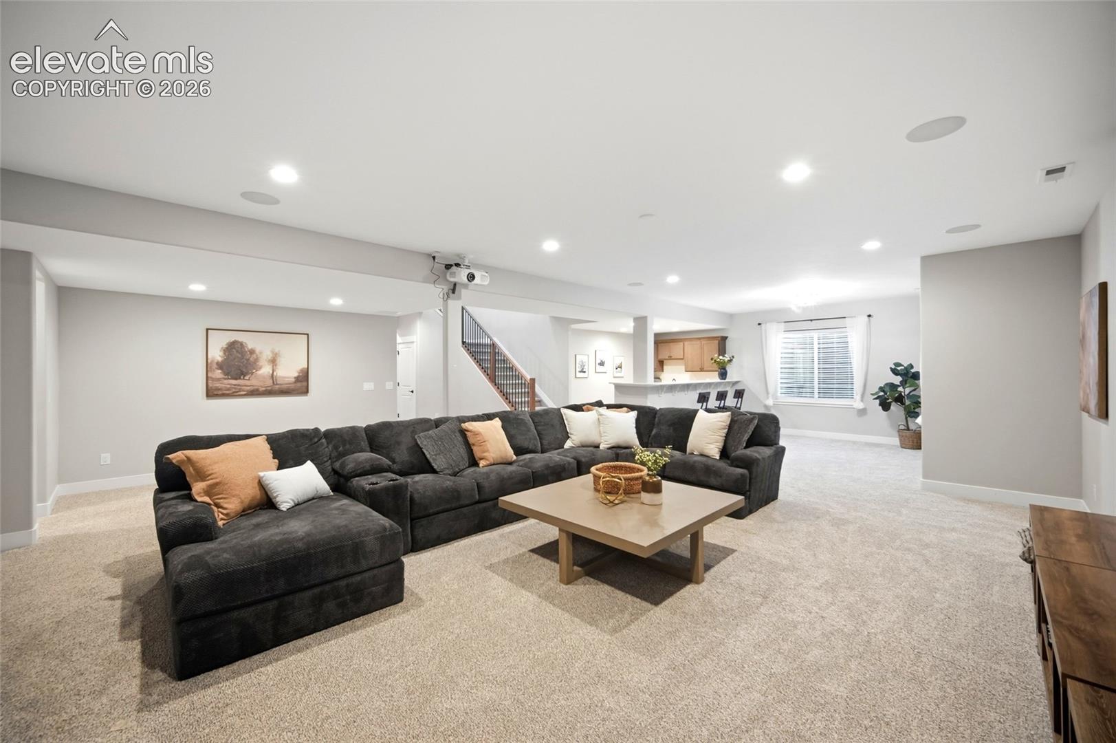 Open-concept floor plan featuring recessed lighting, integrated ceiling speakers, carpeting, a breakfast bar, and a staircase with a wooden handrail