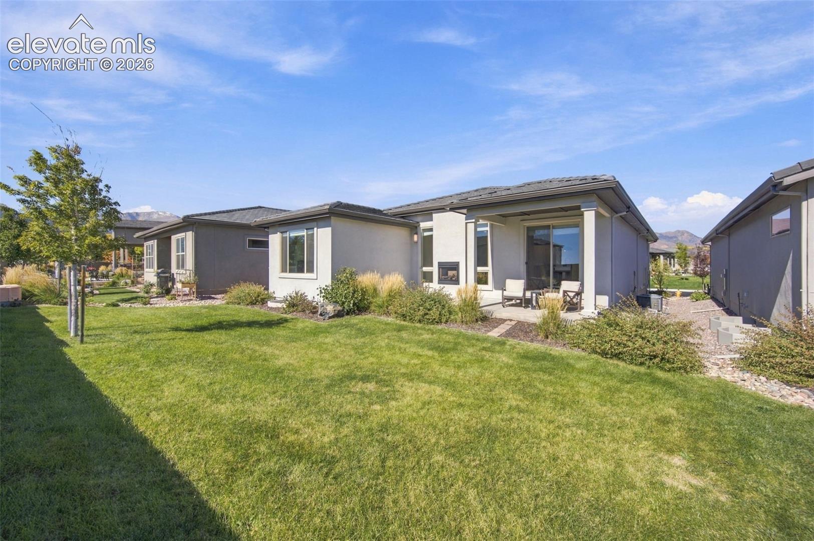 Backyard featuring a covered patio, exterior fireplace, manicured lawn, and professional landscaping